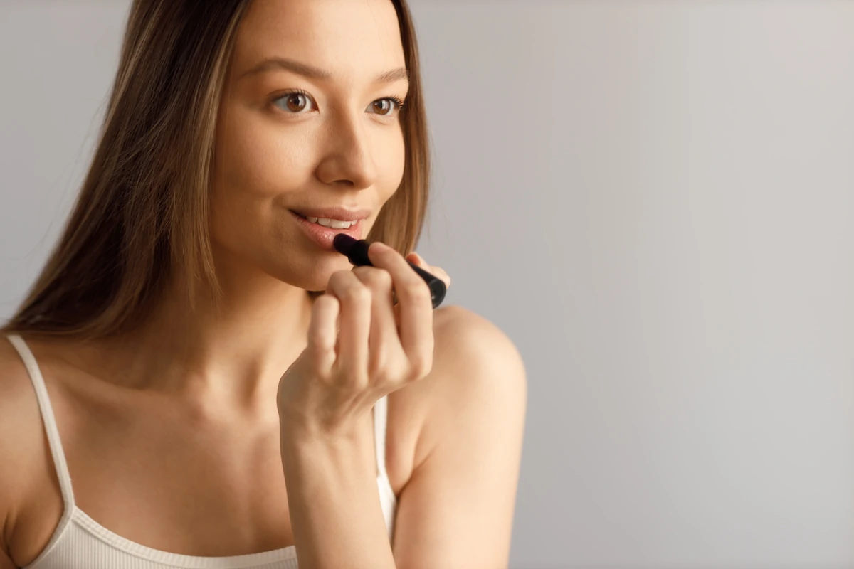 Une une femme peau claire qui applique un rouges à lèvres nude